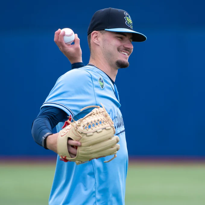 Spencer Giesting smiles while warming up with a light blue uniform top on and a navy cap.