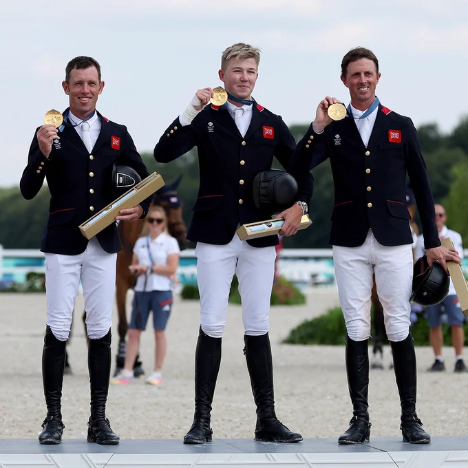 Scott Brash, Harry Charles and Ben Maher stand on the podium holding their gold medals aloft