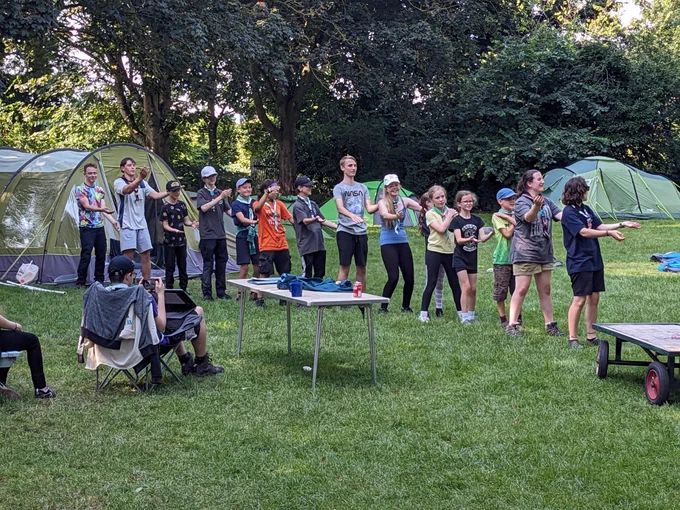 Scouts in a line in front of tents dancing the macarena 