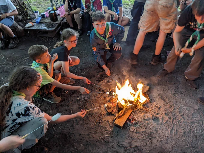 Scouts crouching around a small fire toasting marshmallows 