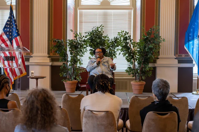 Dr. Allie Martin sitting in a chair on a stage discussing her soundscape composition in front of an audience at the Connecting Communities Digital Initiative (CCDI)'s Summer Fuse 2024 event.