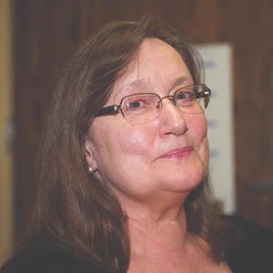 Margot Imdieke-Cross has brown hair and wearing glasses. She is smiling at the camera.