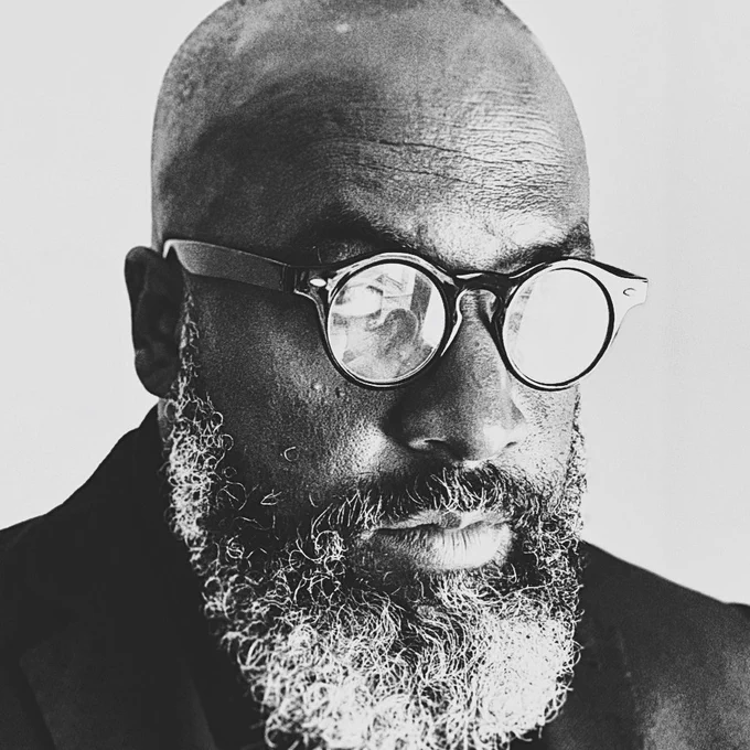 A man with a beard wearing round glasses and a black jacket.