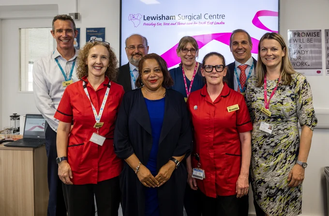 Brenda Dacres standing in front of a screen showing the Lewisham Surgical Centre logo, joined by NHS colleagues