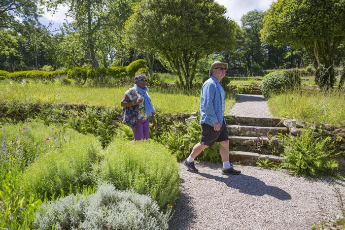 Two people walking on a gravel path through a lush green garden