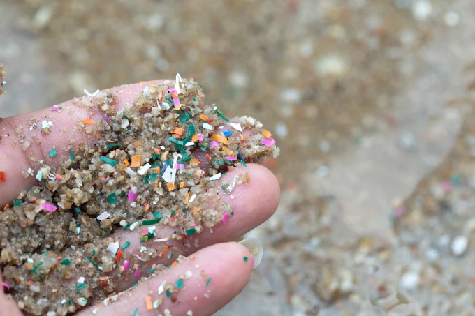 Hand holding microplastics in sand.