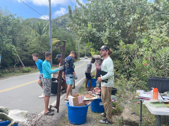 Several people sort trash into large blue buckets by the side of the road.