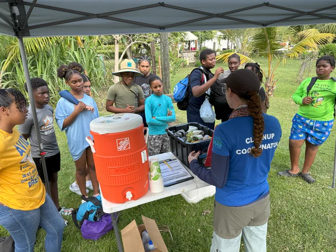 A cleanup coordinator talks to students and volunteers under a canopy.