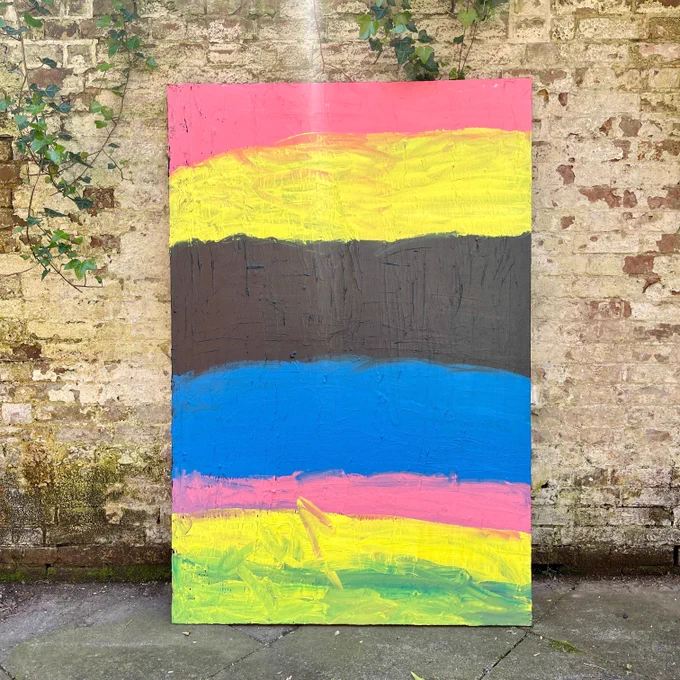 A large canvas painting by Connor Ashley is photographed against a brick wall outside. The painting is abstract with large vertical blocks of colour. The colours are pink, yellow, black, blue, pink, yellow and green.