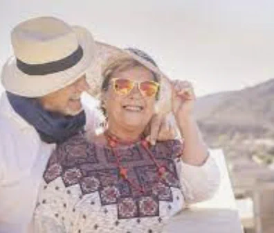 A man and a woman are smiling at each other. The woman is wearing sunglasses and a hat.