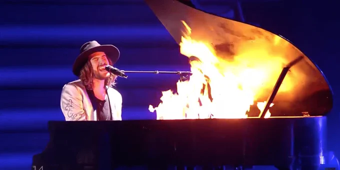 A man performing next to a piano on fire