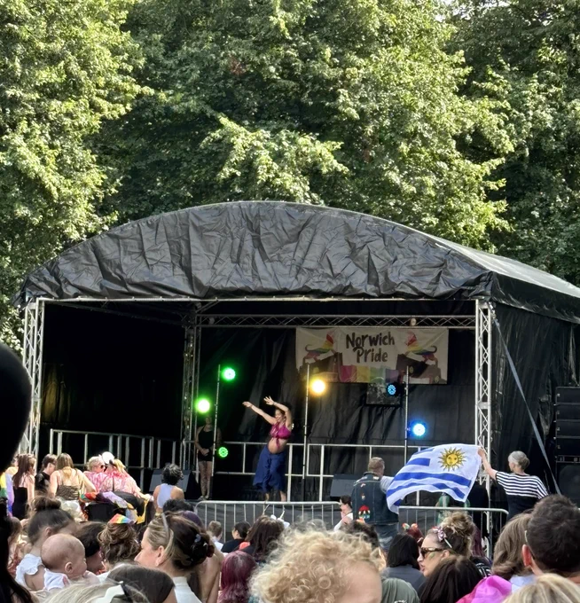 Rosy May on the stage at Norwich Pride, while 2 people at the front wave the flag of Uruguay 🇺🇾