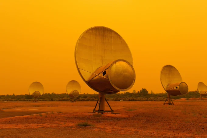 Five telescope dishes of the Allen Telescope Array are seen in their field. The sky in the background is orange due to smoke from the Park Fire.