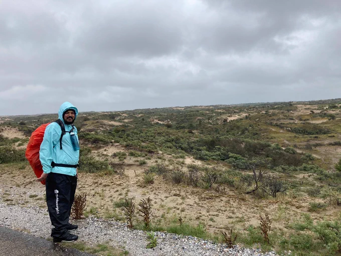 photo from an outdoors durational performance. People are wearing hiking gear and walking on a hill and in the fields