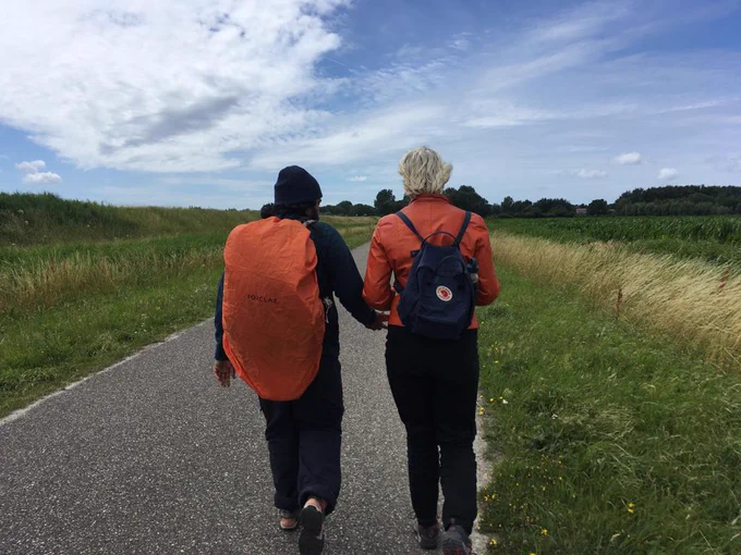 photo from an outdoors durational performance. People are wearing hiking gear and walking on a hill and in the fields