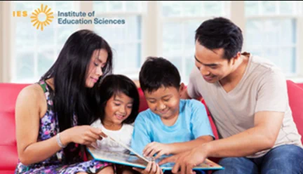 A mother and father sitting with their son and daughter on a sofa reading a story book together. At the top left of the image is the Institute of Education Sciences logo.