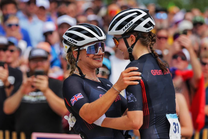 Evie Richards and Ella Maclean-Howell smile and embrace each other as they celebrate finishing the women's cross-country race. 
