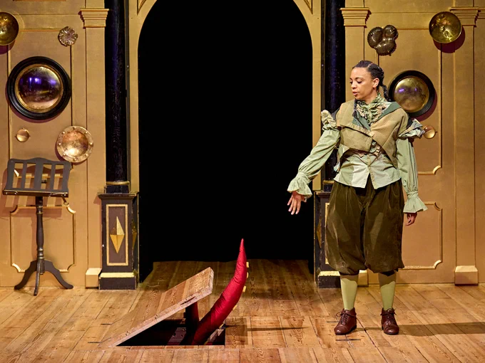 The company of Rough Magic (2024) onstage in the Sam Wanamaker Playhouse - Janet Etuk stood looking at the trapdoor onstage, a red tentacle coming out from it.