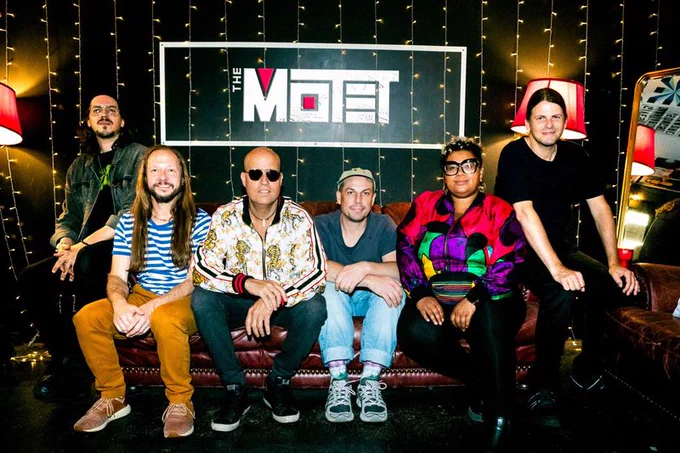 The Motet Band poses for a photo in front of their band name sign. 