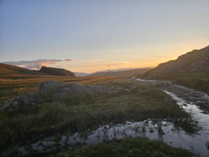 Sunset over Garburn Pass. Standing water I  foreground. Golden glow over fells in distance. 