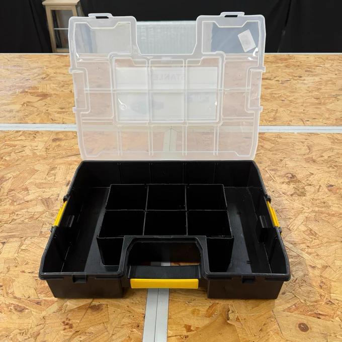 An open, empty Stanley branded tool organizer box with adjustable compartments, displayed on a wooden workbench.