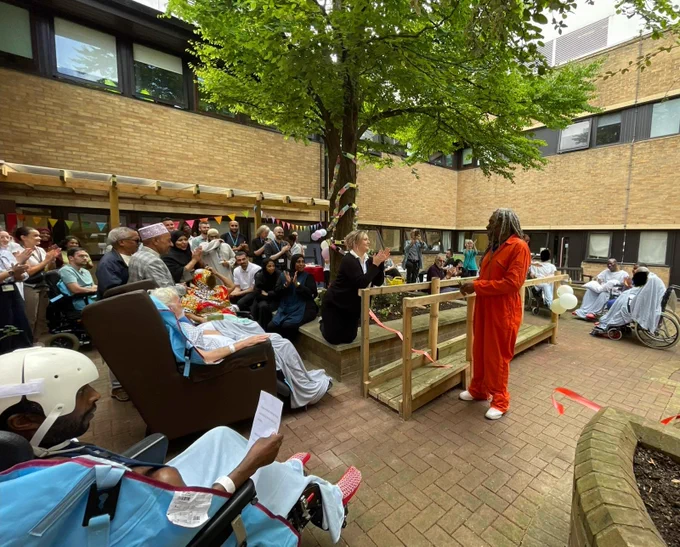 A person standing in a courtyard cutting a ribbon in front of a crowd of medical staff and patients.