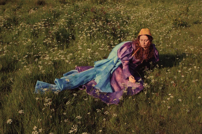 A woman in a satin purple dress and blue shawl is sitting in a field of flowers