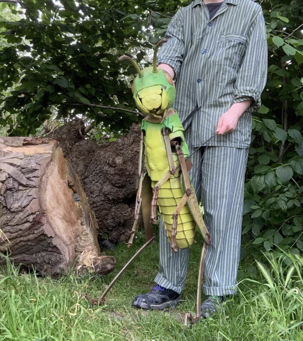 A man holds a large grasshopper structure in the woods