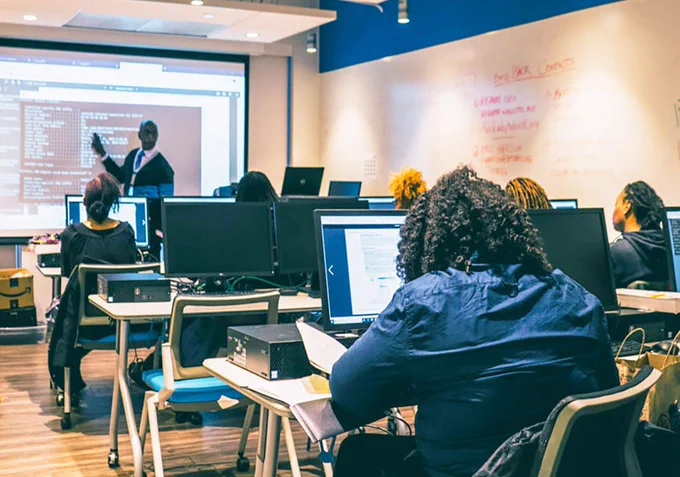 People sitting behind computers in a classroom with a lecturer in the background