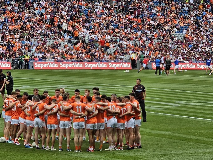 Image shows the Armagh Gaelic team in a huddle during the All Ireland Final 2024 while the crowd watches on