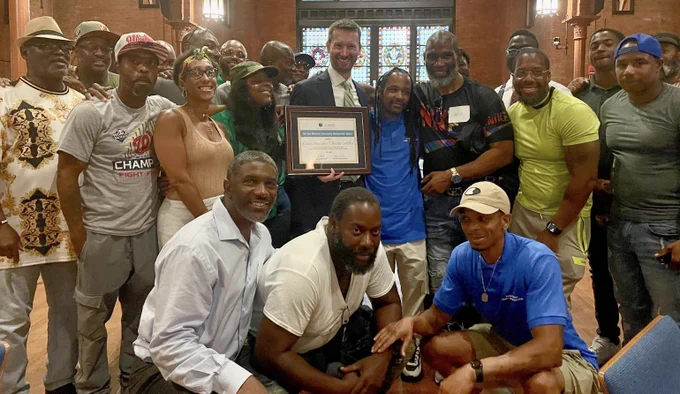 Free Minds members gathered around Councilmember Allen, who holds his framed award in the center of the image. 