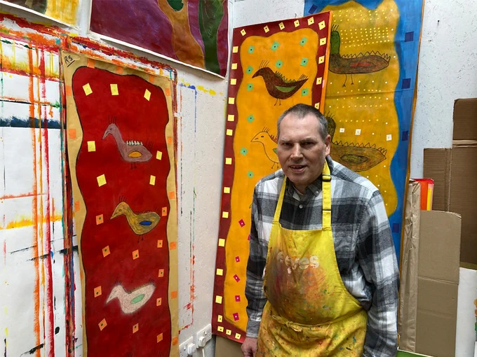 Artist Robin Smith standing next to a series of paintings in the studio.