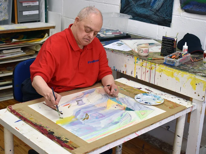 Artist Ali Kamalati sat at a table painting.