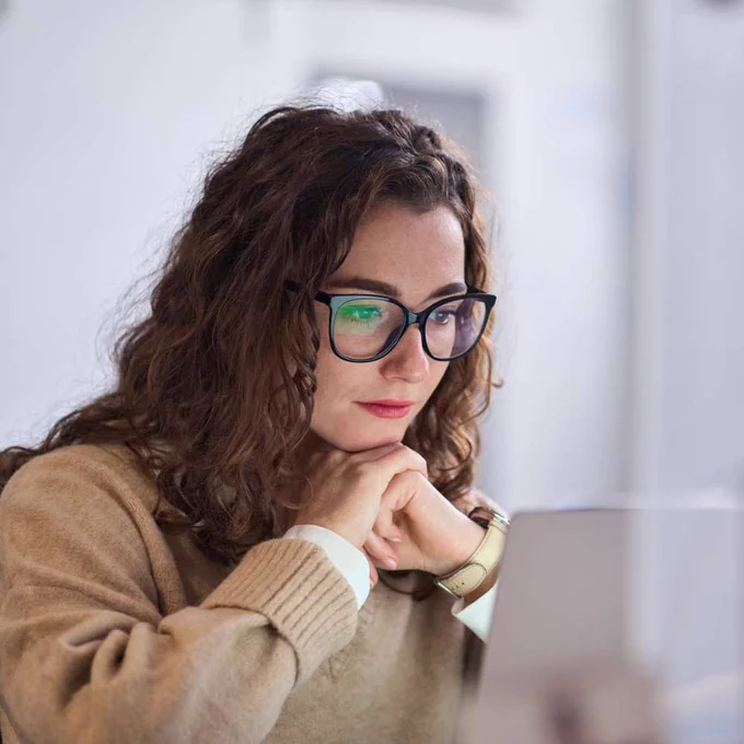 A woman wearing glasses reading something on a laptop.