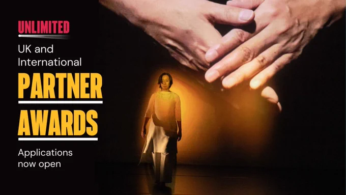 Artist Chisato Minamimura walks towards the audience as a yellow spotlight creates a glow on her. Projected behind her, is a large image of a pair of hands. They're crossing over each other as if the hands are connecting together. They appear to be signing in sign language.  

To the right of this, text reads “Unlimited UK and International Partner Awards. Applications now open.  