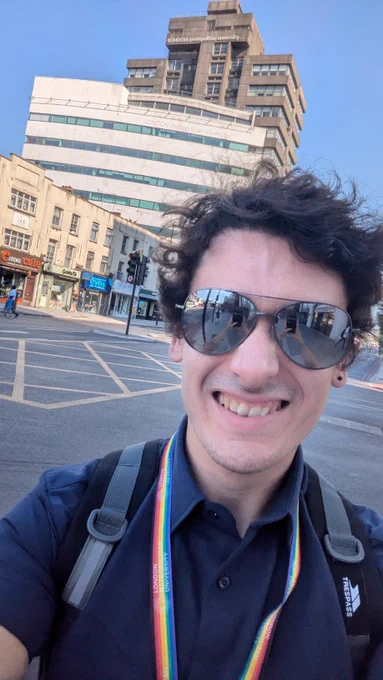 A man wearing sunglasses pulling an excited face in front of the London Metropolitan University Tower building