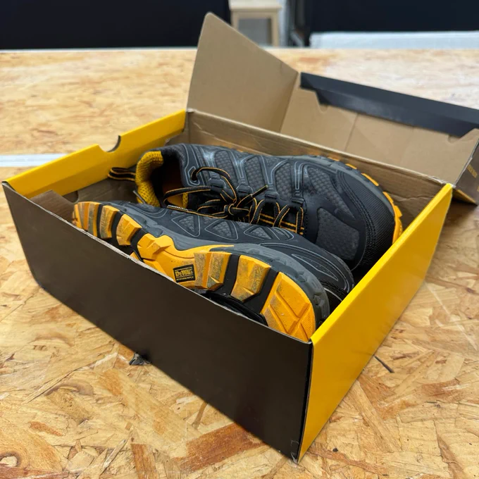 A pair of new Dewalt work boots with distinctive black and yellow colors, displayed in an open box on a wooden surface.