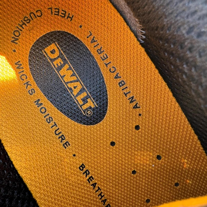 Close-up of aDeWalt shoe tongue label showing the brand name and the features "WITH BOUNCING SOLES" and "ANTIBACTERIAL" embossed on an orange background.