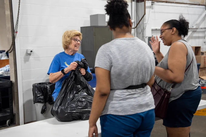 Two women looking at it each other talking while smiling. One women is holding a black plastic bag