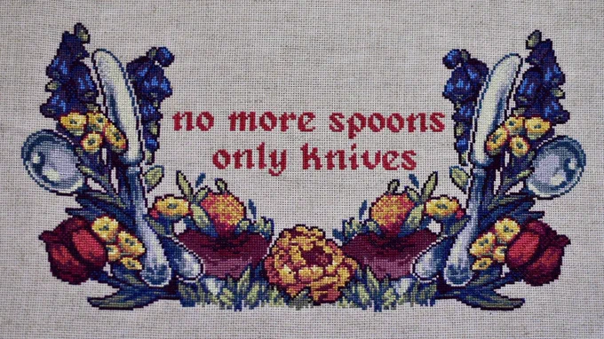 A cross stitch of various flowers and spoons and butter knives. Text in the middle reads, "no more spoons / only knives".
