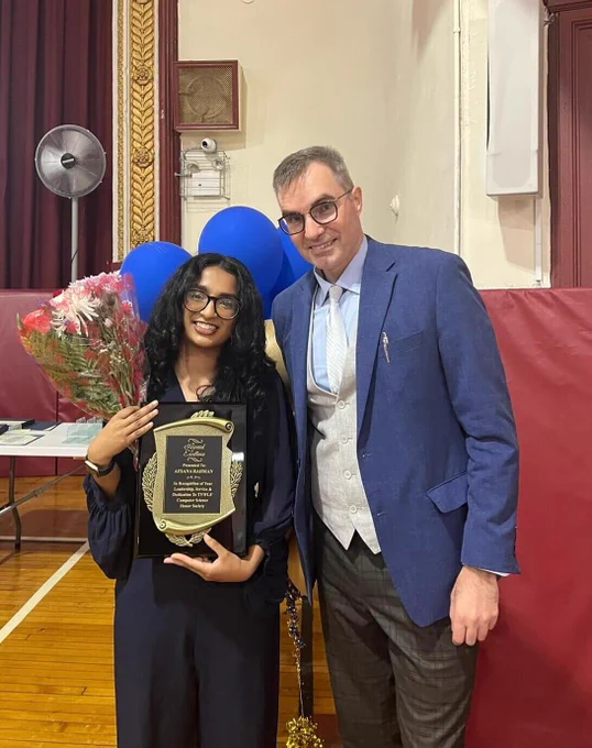  A man stands with a student who is holding a certificate.