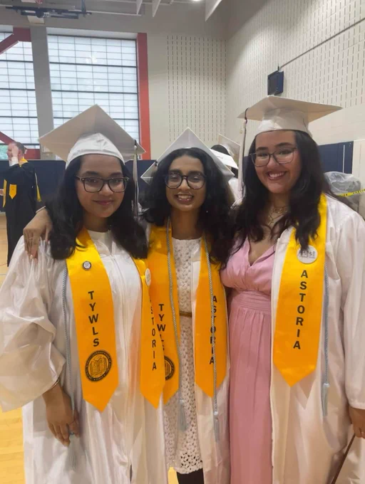 Three students pose in white graduation caps and gowns. 