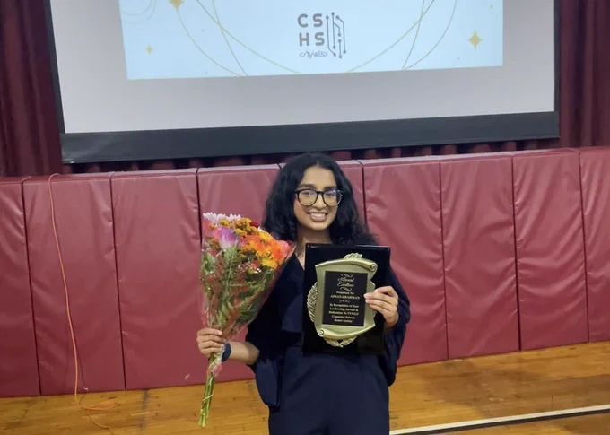 A student poses with a flower and a certificate. 
