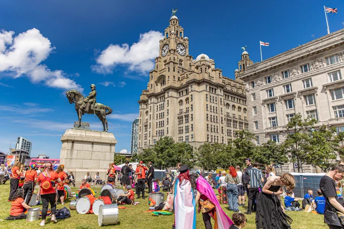 People at Pride in Liverpool festival site on Pier Head. The Edward VII Monument, Royal Liver Building and Cunard Building also feature