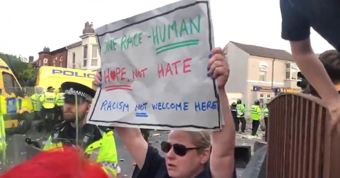 Woman holding sign up "One Race - Human, Hope not Hate, Racism not welcome here"