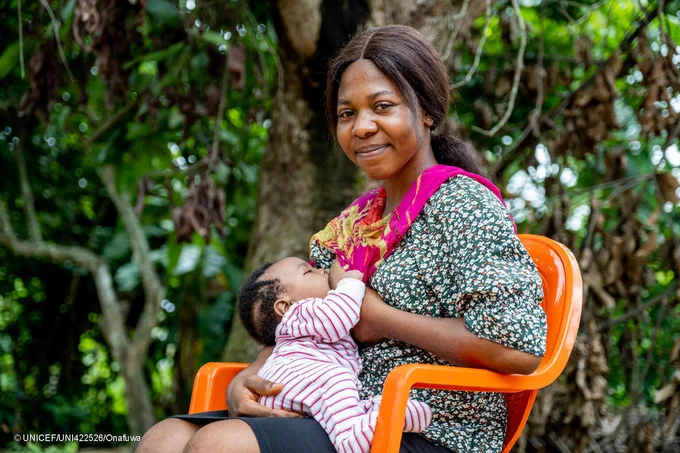 A woman breastfeeds her baby while sitting down on a chair.
