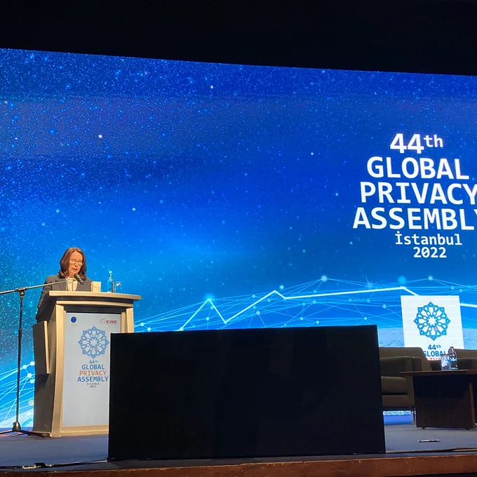 Angelene Falk standing on stage at lectern with screen behind. Text on screen reads ‘44th Global Privacy Assembly Istanbul 2022’