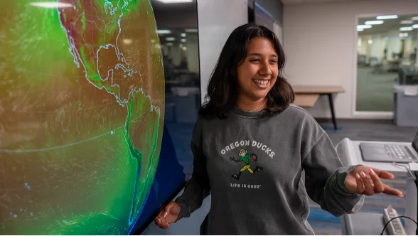 A college student in a classroom stands in front of a screen showing a huge picture of the earth.