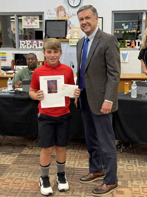 Boy and adult standing in library with boy holding certificate