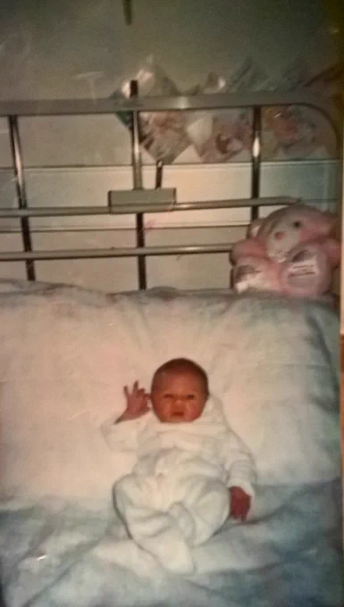 Pic of my daughter in hospital bed waving at the camera only 48hours old pink bear behind her to left on pillow that says its a girl 